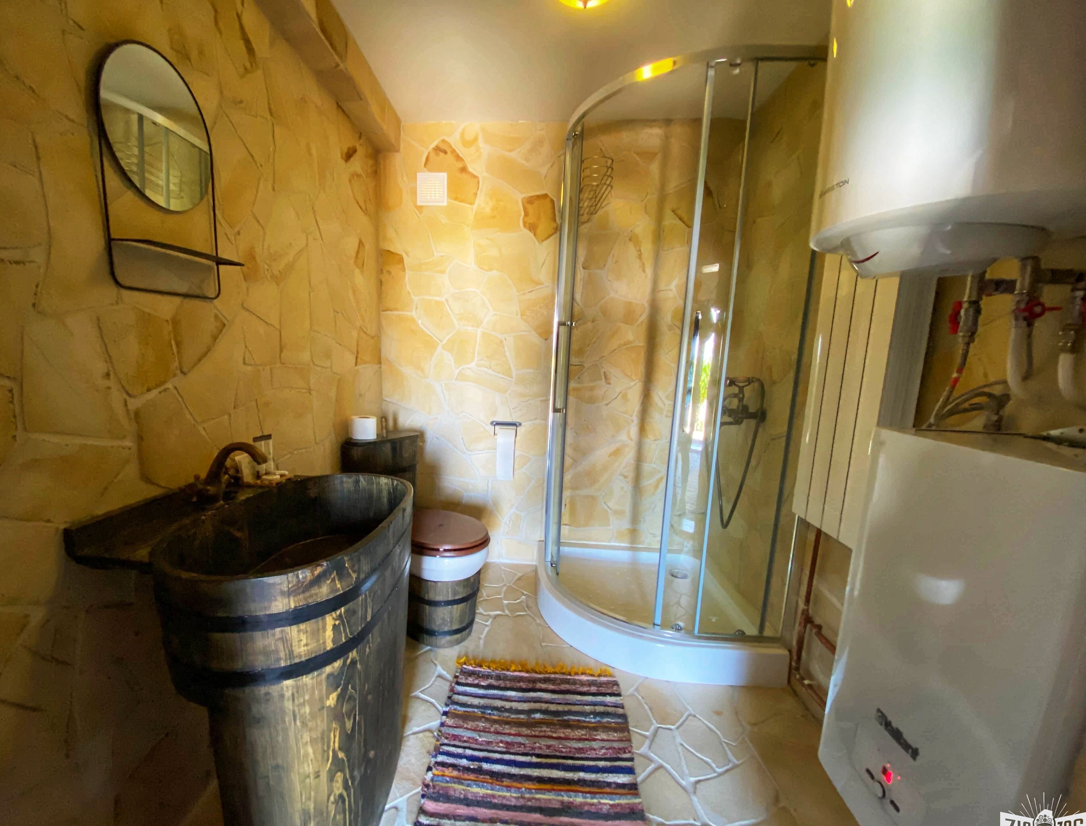 A bathroom with a stone wall, a wooden basin, a glass shower enclosure, and a white cabinet.
