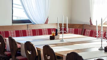 Un espace repas avec une longue table en bois, des bancs recouverts d’un tissu rouge et des bougies blanches.