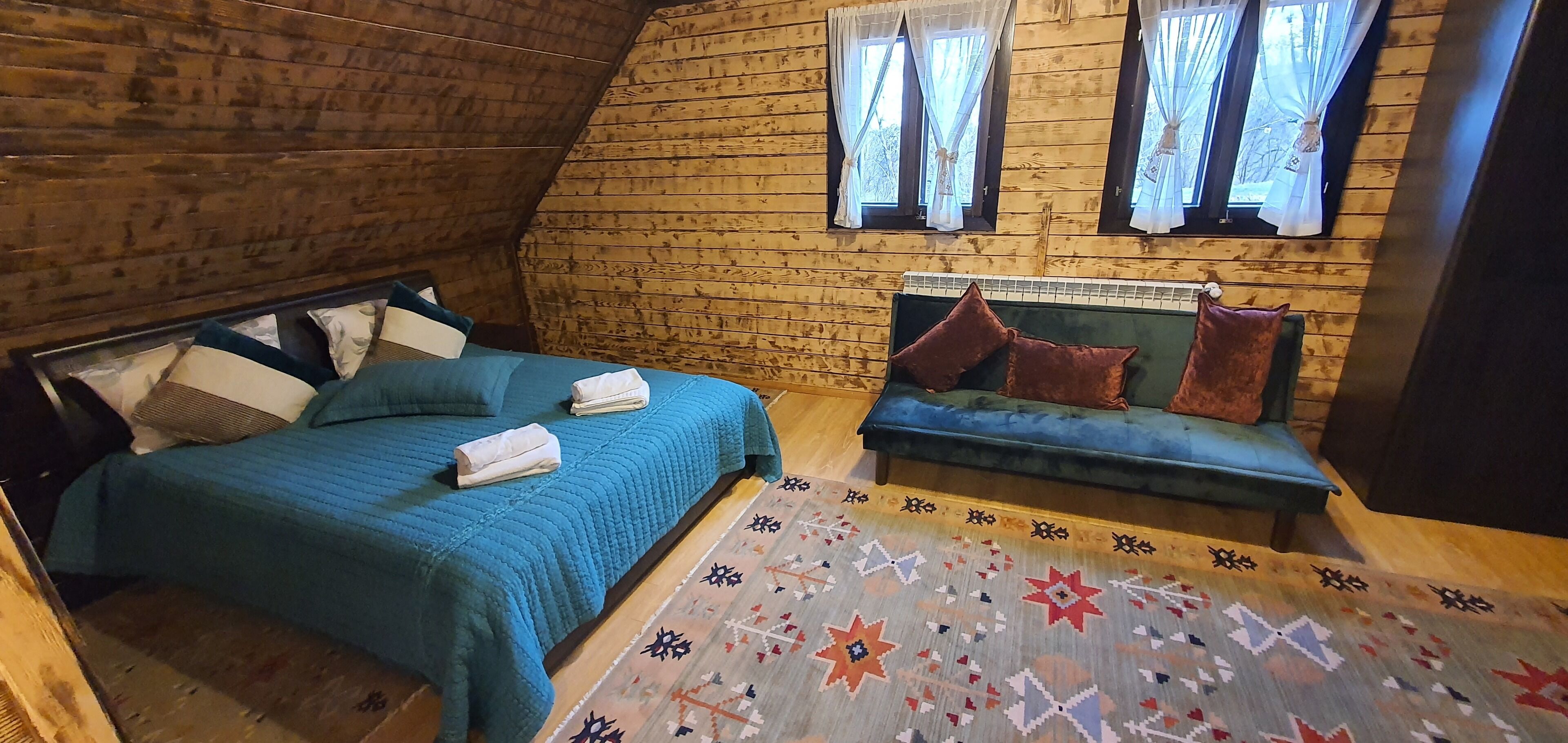 Une pièce chaleureuse avec un plafond en pente, des murs en bois, un lit avec une literie bleue, un banc avec des coussins et un tapis à motifs.