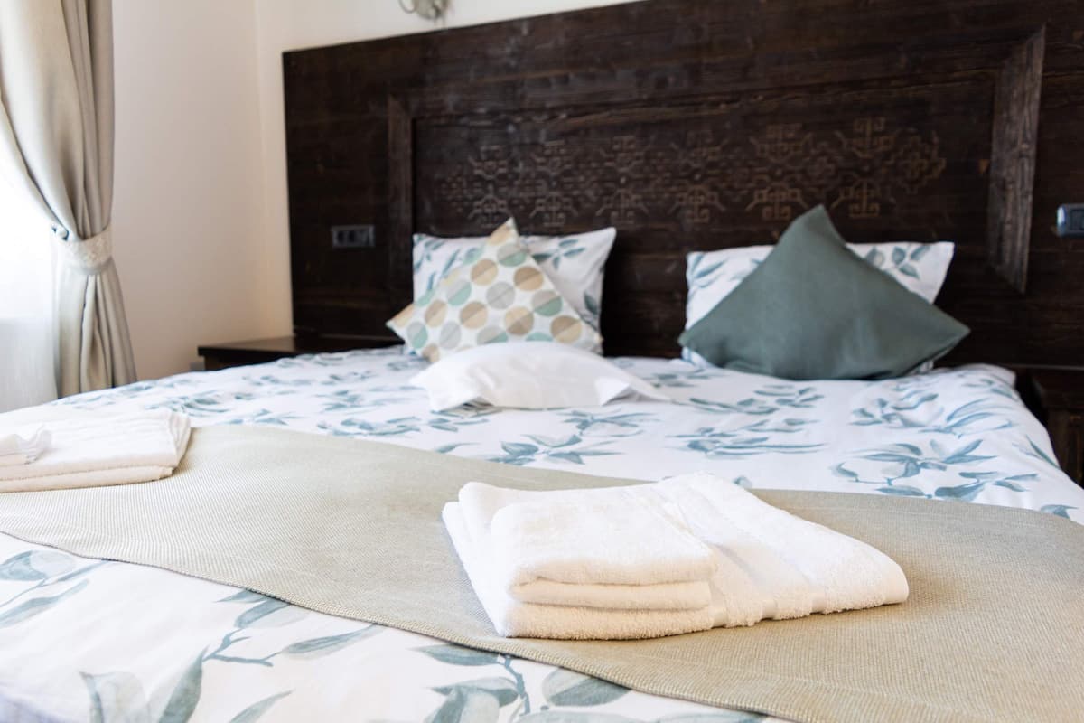 A neatly made bed with a floral bedspread, a wooden headboard, and a set of folded towels.