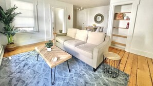 A living room with a beige sofa, a wooden coffee table, a blue rug, and a small round side table. - Historical 1st Floor 3BR APT Brunswick @ Bowdoin (Brunswick)