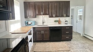 A modern kitchen with dark wooden cabinets, a built-in microwave, and a dishwasher. - Historical 1st Floor 3BR APT Brunswick @ Bowdoin (Brunswick)