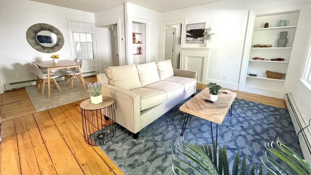 A modern living room with a beige sofa, a coffee table, and a dining area with a table and chairs. - Historical 1st Floor 3BR APT Brunswick @ Bowdoin (Brunswick)