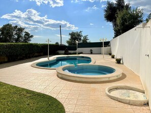 Une piscine divisée en deux zones distinctes, entourée d’une terrasse dallée et d’une haie basse.