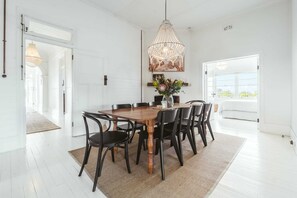 Een eetgedeelte met een houten tafel, zwarte stoelen, een kroonluchter en een vaas met bloemen.