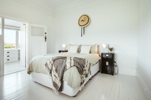 Een slaapkamer met een bed, nachtkastjes, een wandklok en een deur die leidt naar een balkon.