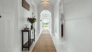 A hallway with a woven rug, a dark console table with a vase of flowers, and a large woven light fixture. - 'Mayfield' - Luxury Farmhouse with Pool (Mayfield)