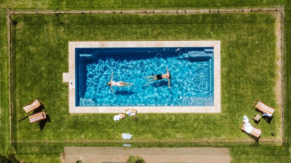 An aerial view of a rectangular swimming pool surrounded by grass, with two lounge chairs and a towel on the ground. - 'Mayfield' - Luxury Farmhouse with Pool (Mayfield)