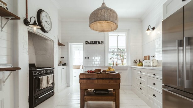A kitchen with white cabinetry, a wooden bench, a stove, and a large hanging light fixture. - 'Mayfield' - Luxury Farmhouse with Pool (Mayfield)
