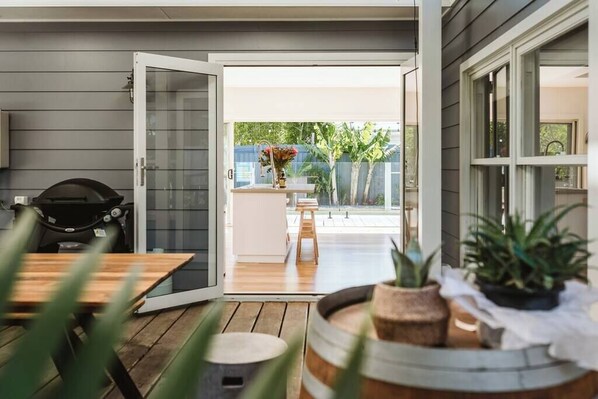 An open patio with a wooden table, a grill, and potted plants.
