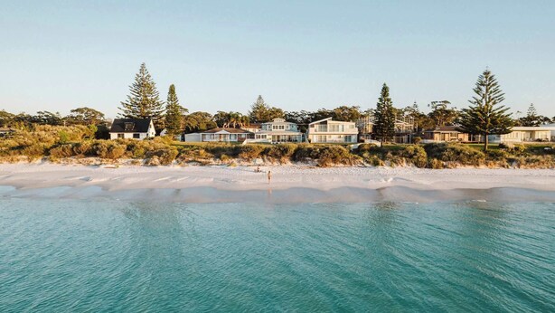 Une propriété située en bord de mer, comprenant plusieurs maisons, une plage de sable et une eau d’un bleu cristallin.