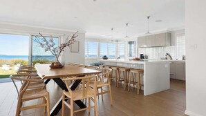 Une cuisine moderne dotée d’un îlot central, de chaises en bois et de grandes fenêtres offrant une vue sur la mer.