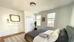 Ein Schlafzimmer mit einem Bett, einem großen Spiegel, einer Tür und Fenstern.