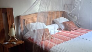 Un lit doté d’une moustiquaire, d’une tête de lit en bois et d’oreillers.