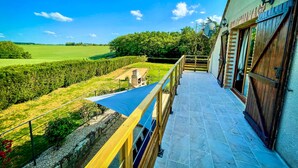 A balcony with a view of a green field and trees, a stone structure, and a building with a wooden door and window shutters. - Villa Cocorico (45) 30 pers-piscine-1h30 Paris (Chantecoq)