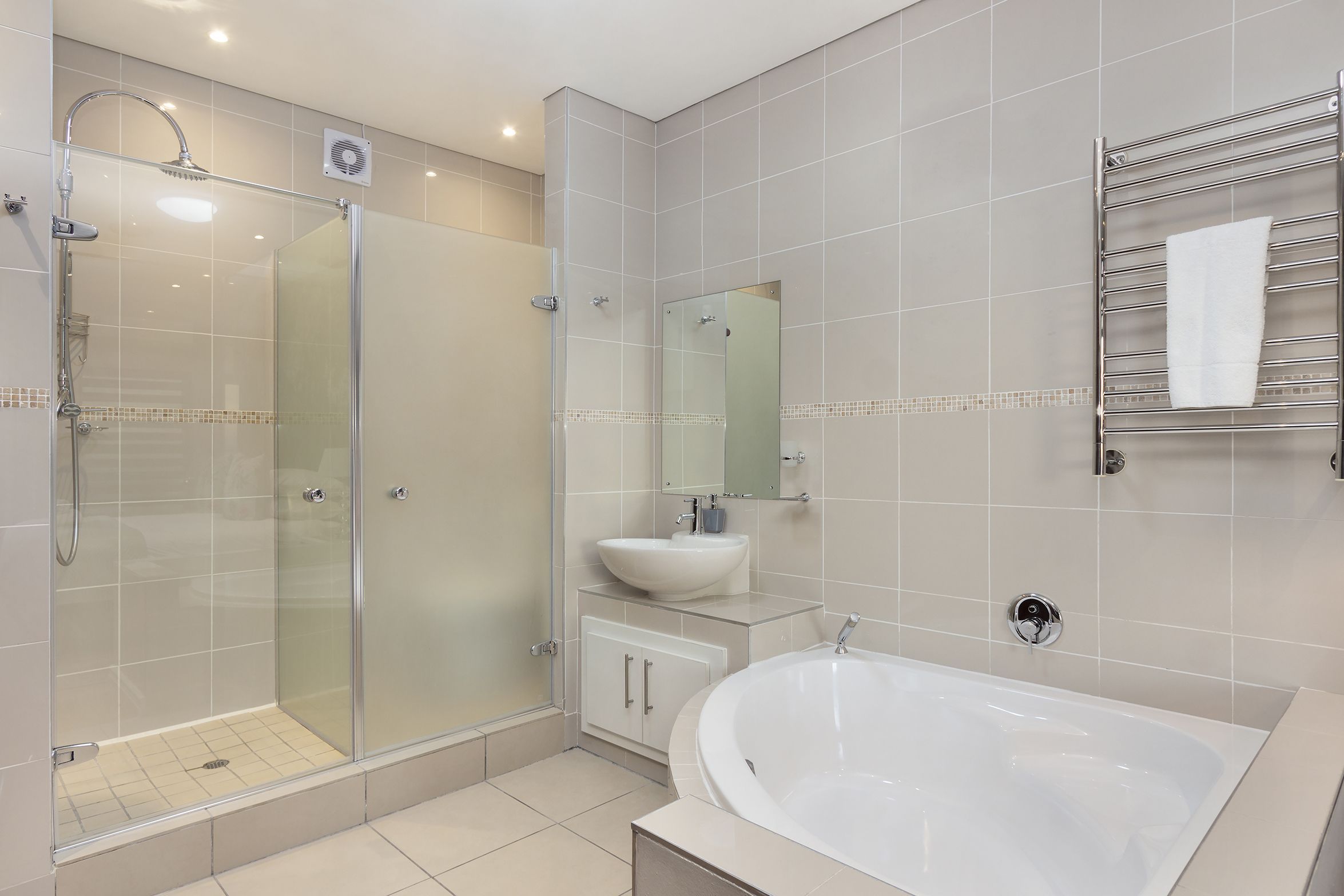 Un baño moderno con ducha de vidrio, bañera independiente y tocador con lavabo y espejo.