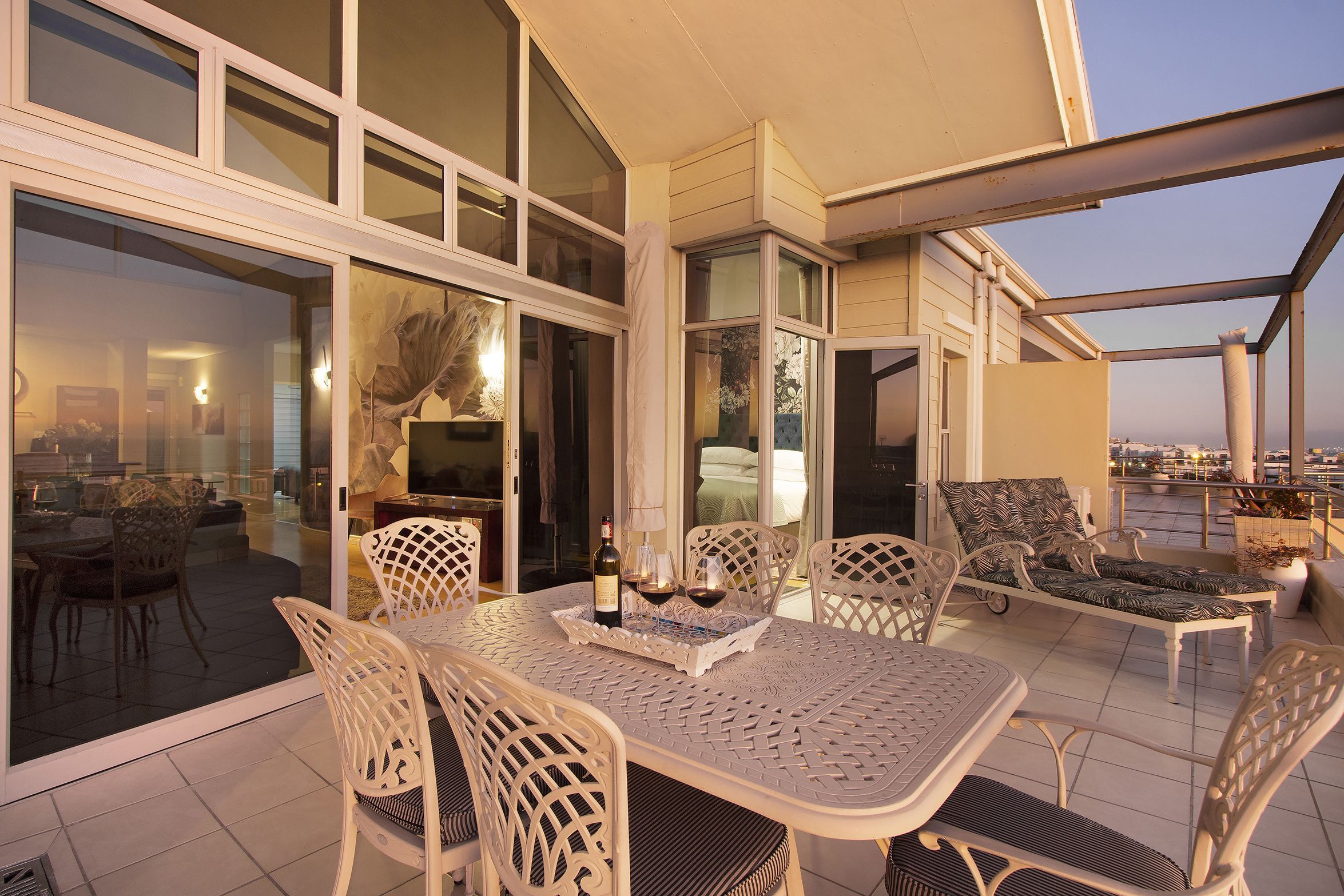 Un patio exterior con una mesa y sillas para comer, un sillón de descanso y vistas de la ciudad.