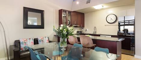 A modern kitchen with a glass dining table, blue chairs, and a vase of flowers.