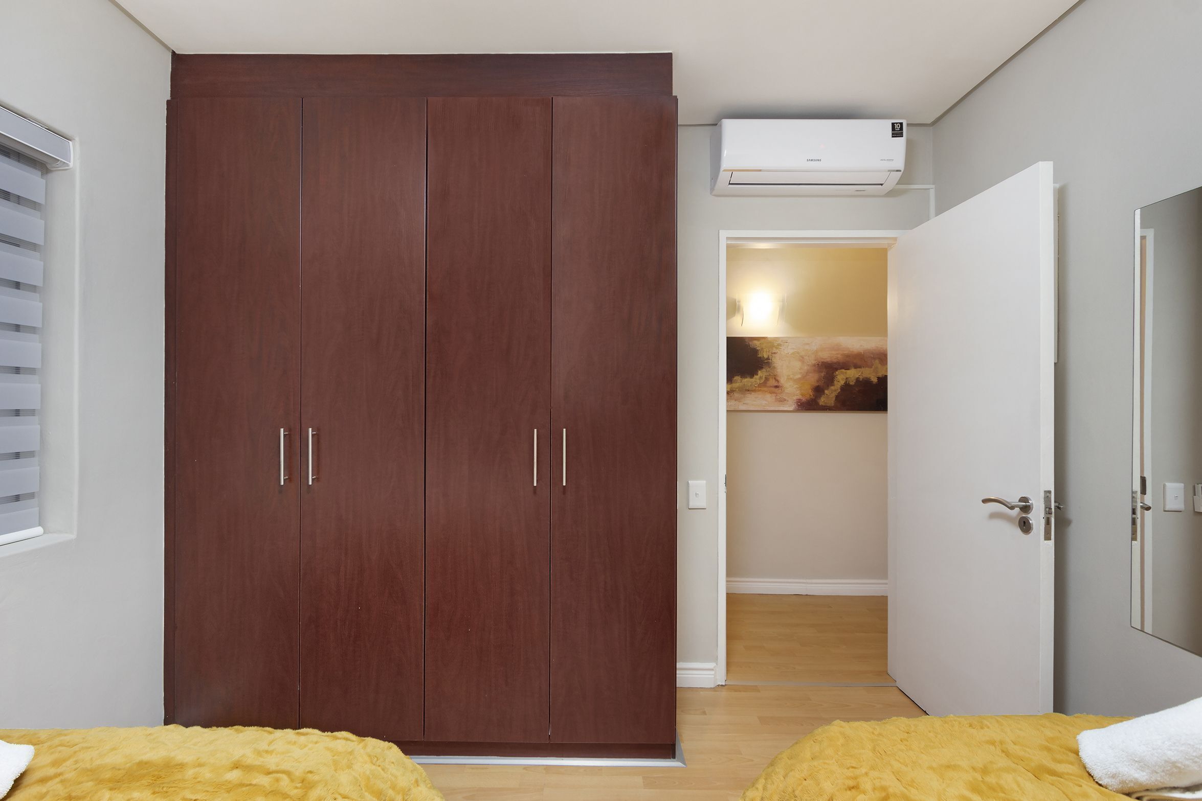 Un dormitorio con un armario grande, una cama con una colcha amarilla y una puerta blanca.