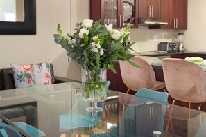 A dining table with a clear glass vase containing white flowers and green foliage.