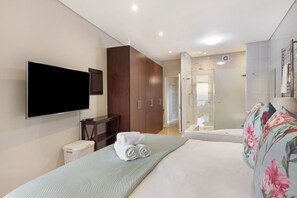 A modern hotel room with a flat-screen TV, a large bed, a wardrobe, a shower area, and a bathtub.