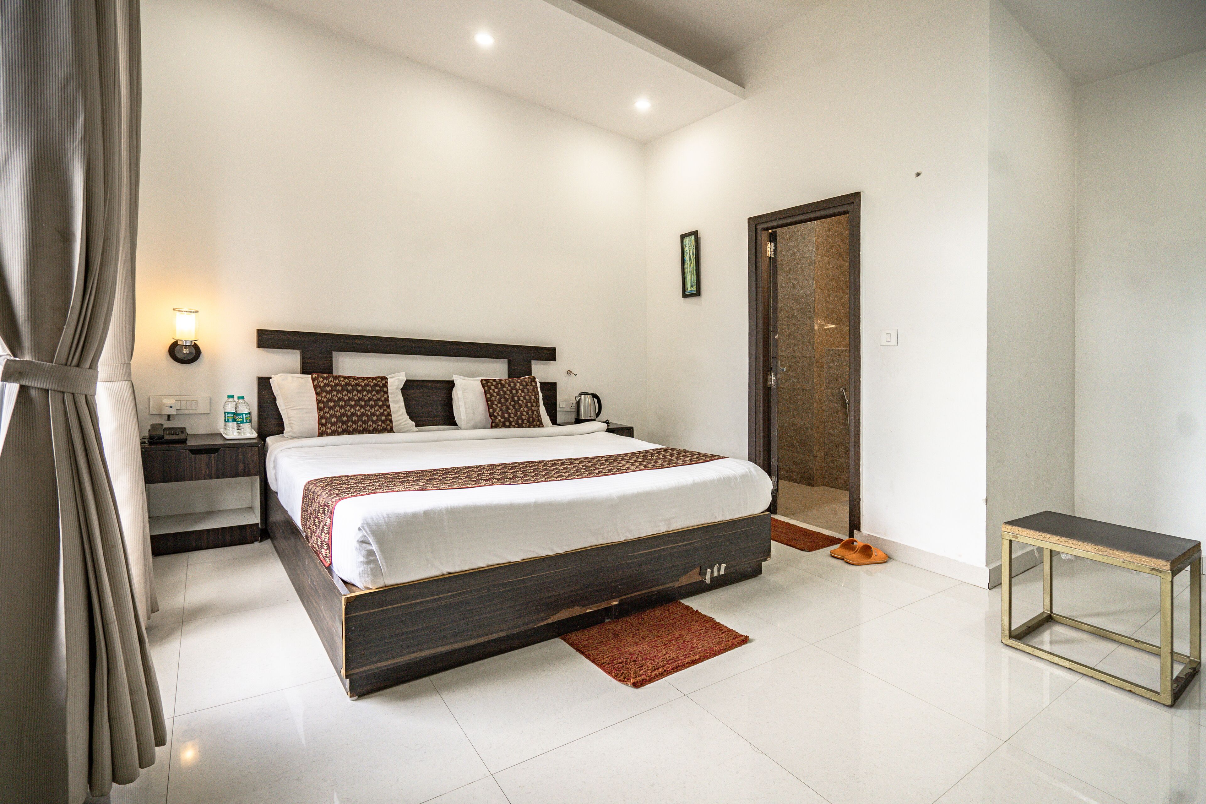 Une chambre moderne avec un grand lit, des tables de chevet, une commode, une lampe de chevet, une porte et une petite table.