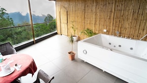 Een moderne badkamer met een ruime badkuip, een bamboewand en uitzicht op een bergachtig landschap.