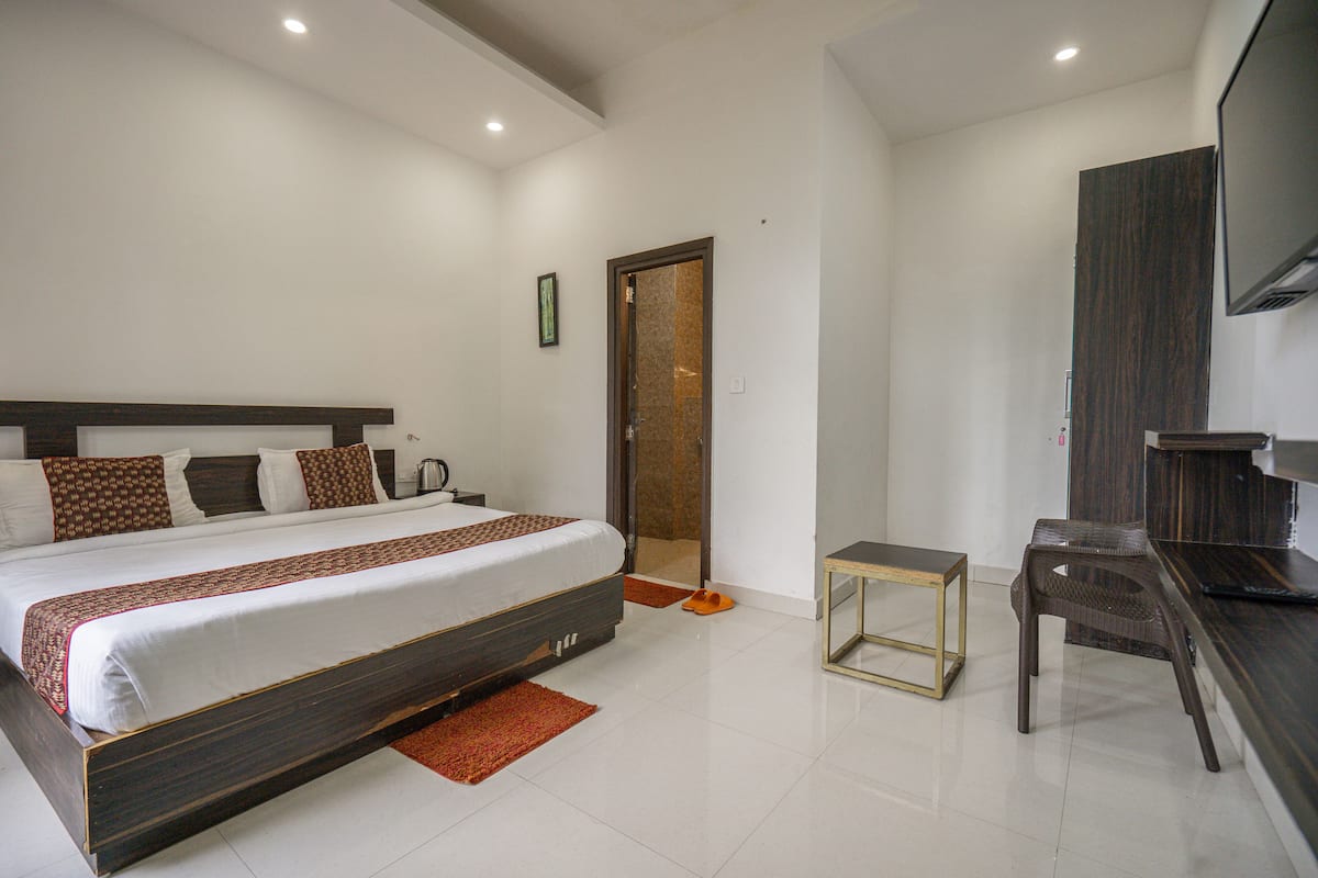 A bedroom with a large bed, a small table, a chair, a TV, and a door leading to another room.