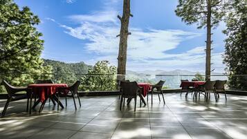 An outdoor dining area with tables and chairs, overlooking a mountainous landscape.