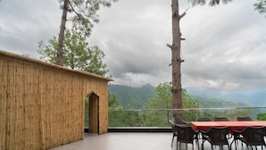 Een bamboestructuur met een tafel en stoelen op een balkon met uitzicht op een bergachtig landschap.