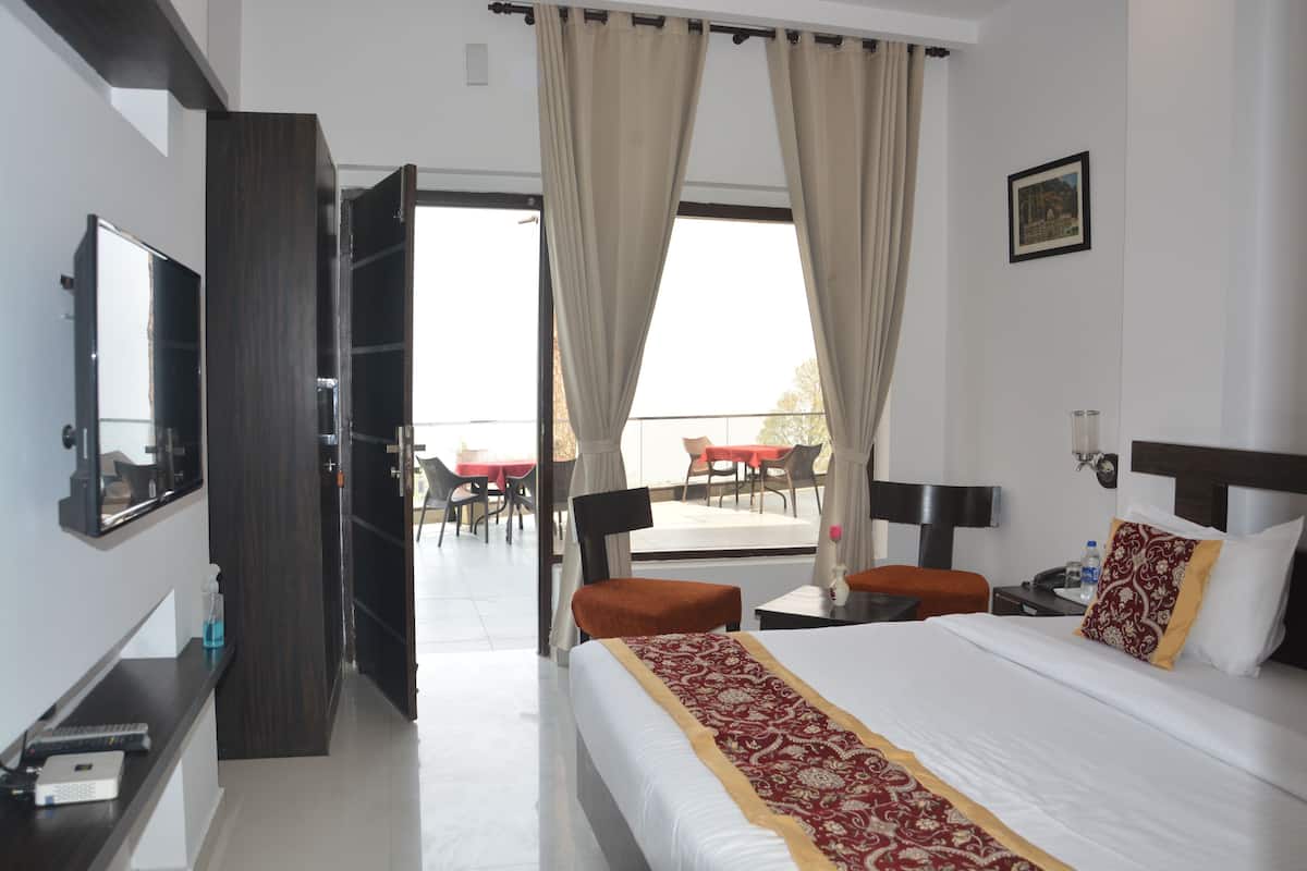 A hotel room with a bed, a desk, a chair, a TV, and a balcony with outdoor seating.