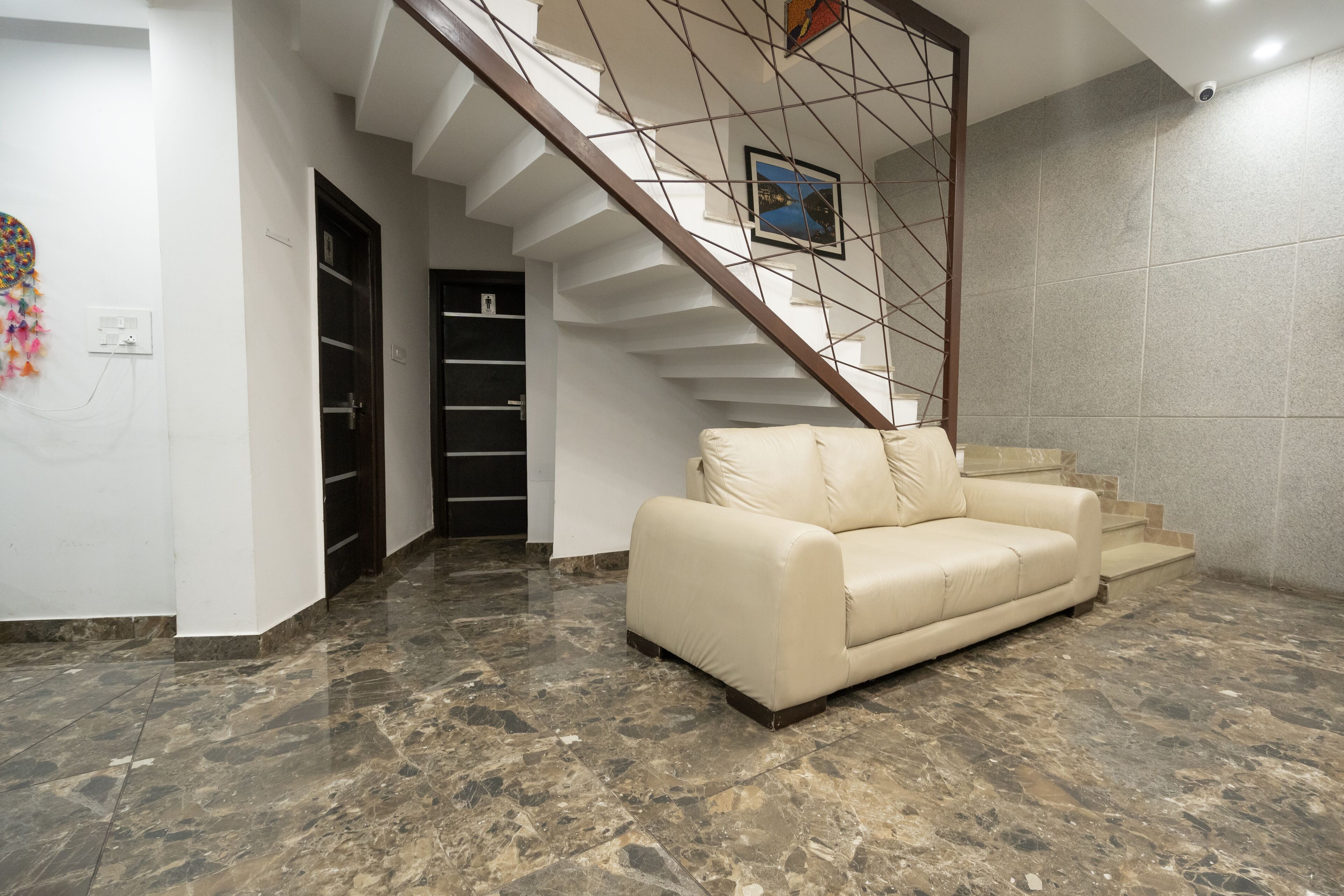 Una sala de estar moderna con piso de mármol, un sofá color beige y una escalera con barandilla de madera.
