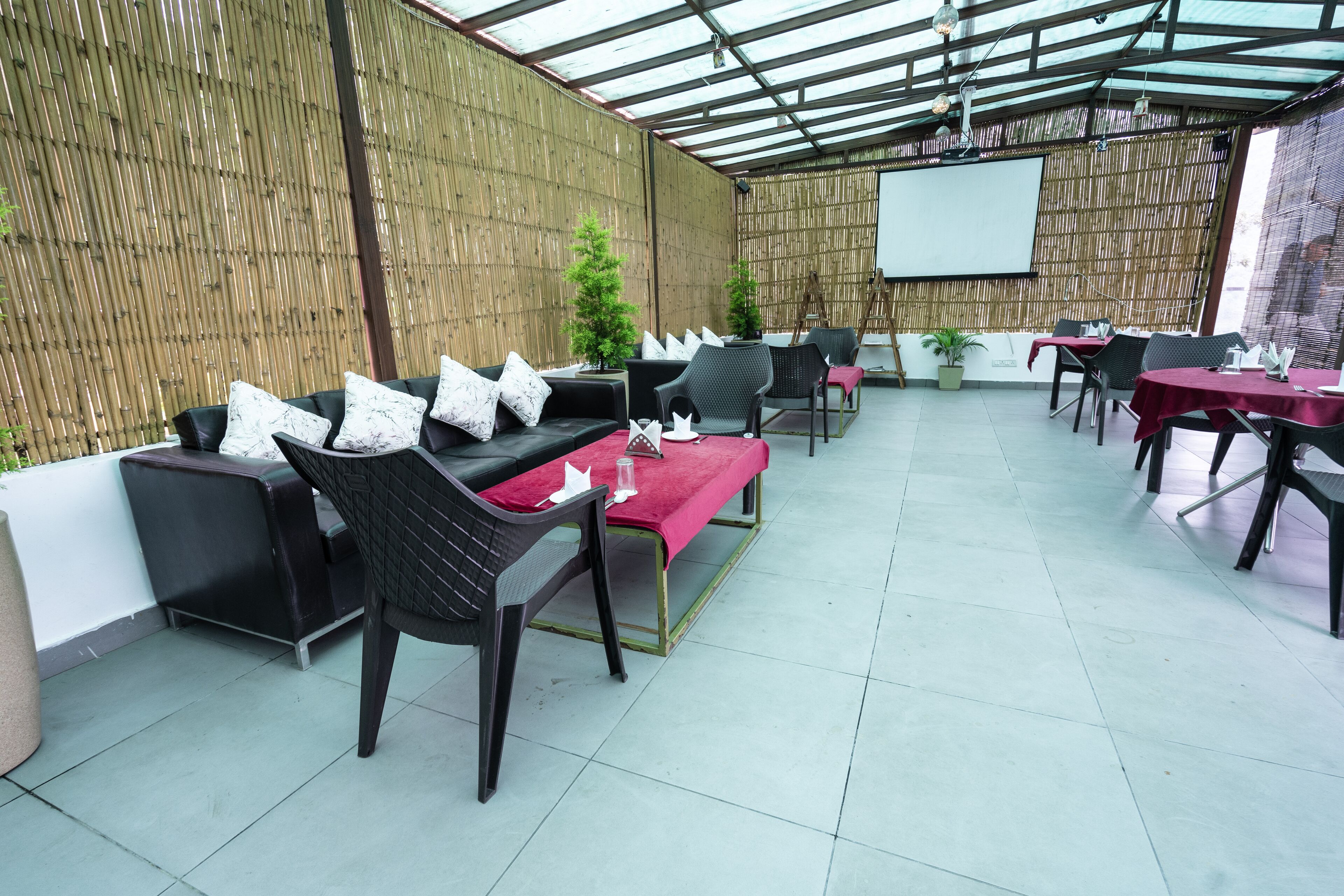 A covered outdoor seating area with black sofas, red cushions, and black chairs.
