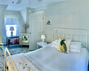 A bedroom with a bed, a chair, a nightstand, a lamp, a window with curtains, and a door.