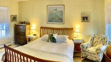 A bedroom with a wooden bed, two bedside tables with lamps, a floral armchair, and a ceiling fan.