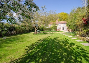 Stroll through the beautifully maintained garden, featuring a variety of trees and flowering plants, to the traditional building with a pitched roof.