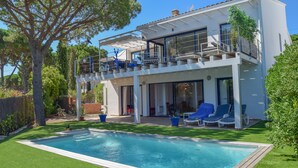 Ett modernt hus i två våningar med en swimmingpool, utomhusmöbler och en balkong med utsikt över poolen.