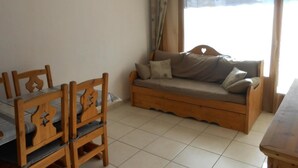 A room with a wooden sofa, a dining table with chairs, and a large window with curtains.