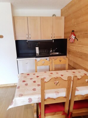 A compact kitchen with wooden cabinets, a black countertop, and a small refrigerator.