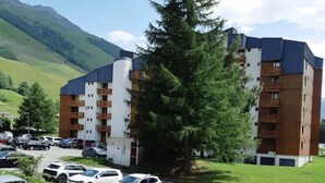 A multi-story hotel with a parking lot, surrounded by greenery and mountains.