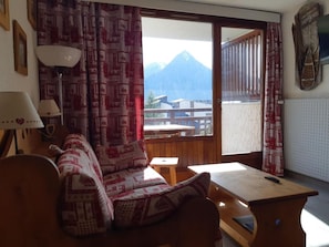 A room with a sofa, a table, a lamp, and a view of mountains through a window.