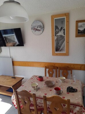 A dining area with a table set for two, a clock, and framed photographs on the wall.
