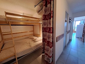 A bunk bed room with a curtain, a door, and a hallway leading to a kitchen area.