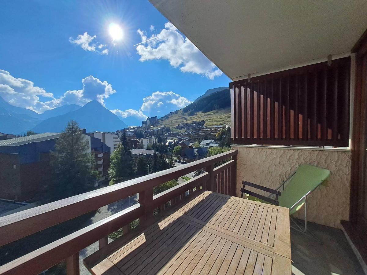 A balcony with a wooden floor, a green chair, and a view of a town and mountains.