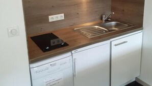 A compact kitchen with white cabinets, a built-in microwave, a dishwasher, and a wooden countertop.