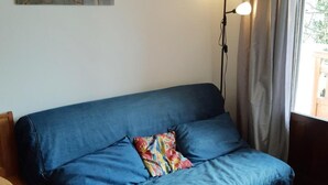 A blue sofa with a colorful pillow, a floor lamp, and a painting on the wall.