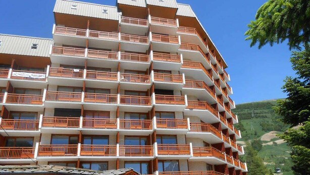 A multi-story hotel with balconies, a ski slope in the background, and a mountain view.