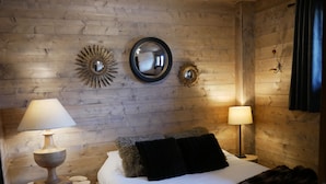 Un dormitorio acogedor con pared de madera, una cama con una manta de piel, dos lámparas de noche y espejos decorativos.