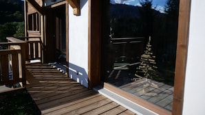 Una terraza de madera que da a un amplio ventanal con vistas a un bosque y montañas.