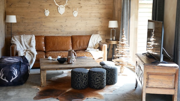 Una habitación acogedora con pared de madera, un sofá de cuero marrón, una mesa de centro y un televisor sobre un mueble de madera.